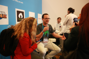 Ein Interview mit Menschen mit Mikrofonen und einer Kamera, mit Personen im Vordergrund und einem Banner links, während der Hintergrund klar ist.