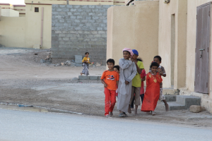 Eine Gruppe strahlender Kinder, die vor Gebäuden, Wasser, Felsen und einer Straße stehen.