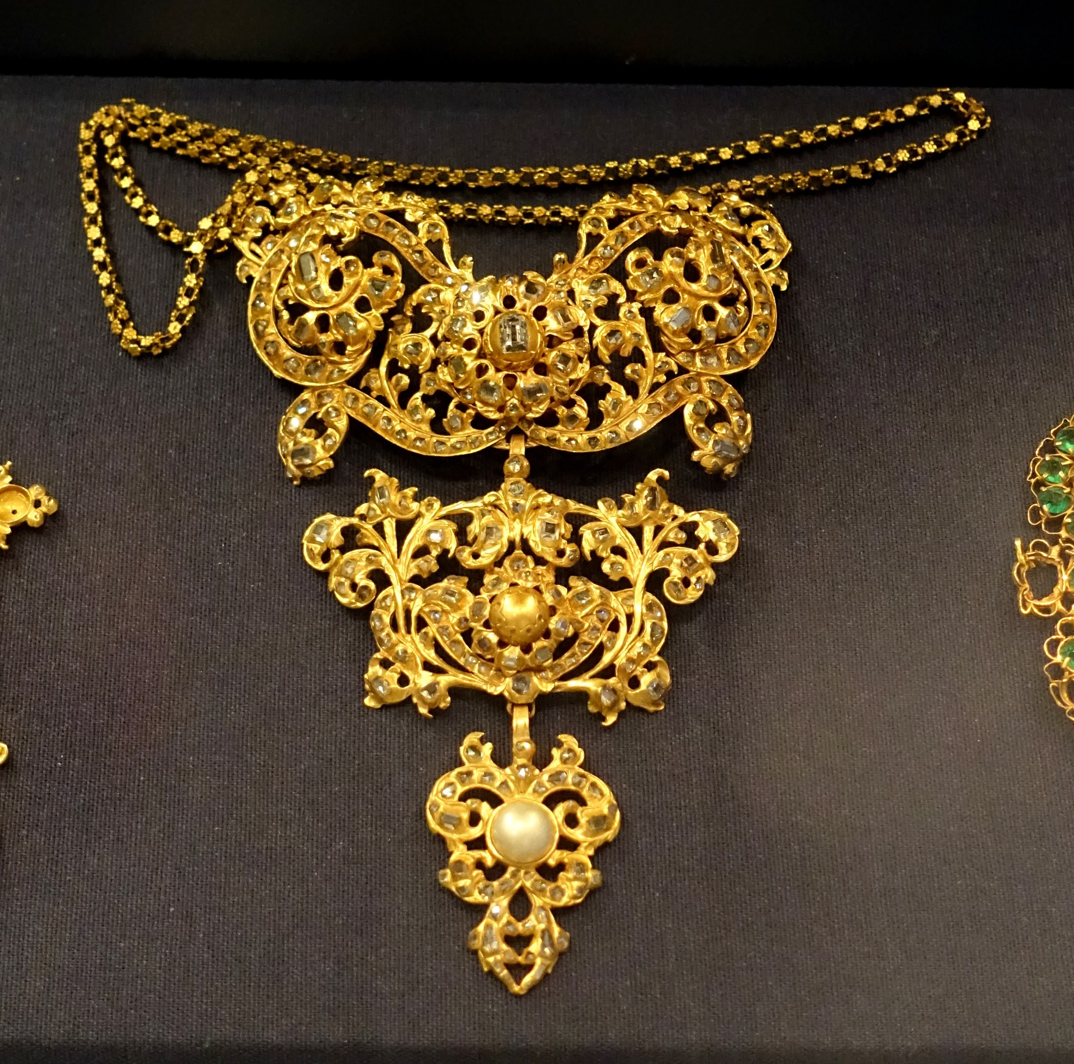 Eine goldene Kette und ein Ohrring-Set mit detaillierten Verzierungen, die im Museum ausgestellt sind, der Schmuck glänzt im Licht.