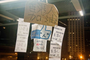 Eine Gruppe von Menschen steht vor einem Gebäude in der Nacht, beleuchtet von Stadtlichtern, mit mehreren Schildern an der Decke, die wahrscheinlich gegen eine Regierungsentscheidung zum Verbot von Social Media protestieren.