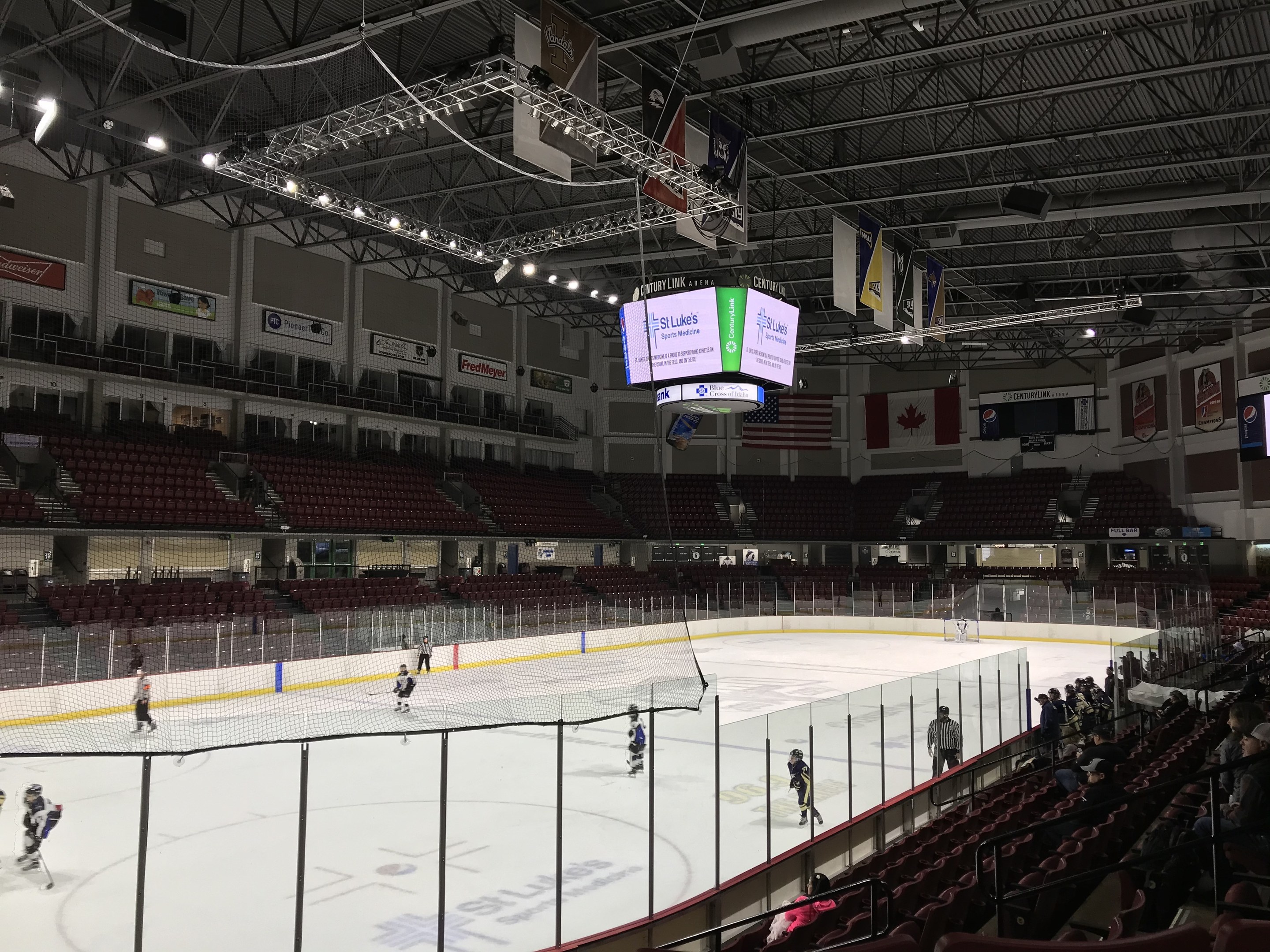 Ein Hockey-Spiel in einer großen Arena mit einem zentralen Netz, Zuschauern auf beiden Seiten, Deckenleuchten und Trägern sowie Bannern an den Wänden, identifiziert als St. Louis Blues Arena.