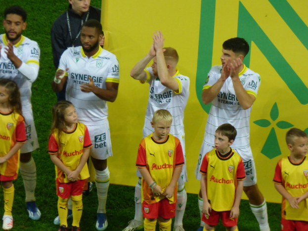 Eine Gruppe von Fußballspielern in Uniformen, die auf einem Ligue 1 Feld klatschen und einen Sieg feiern.