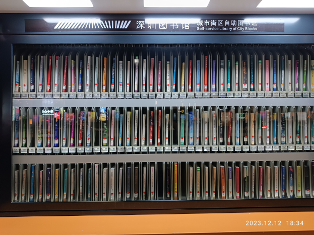 Eine Bibliothek mit hohen Bücherregalen, beleuchtet von Deckenlampen, mit einer Tafel mit Text und einem Wasserzeichen unten.