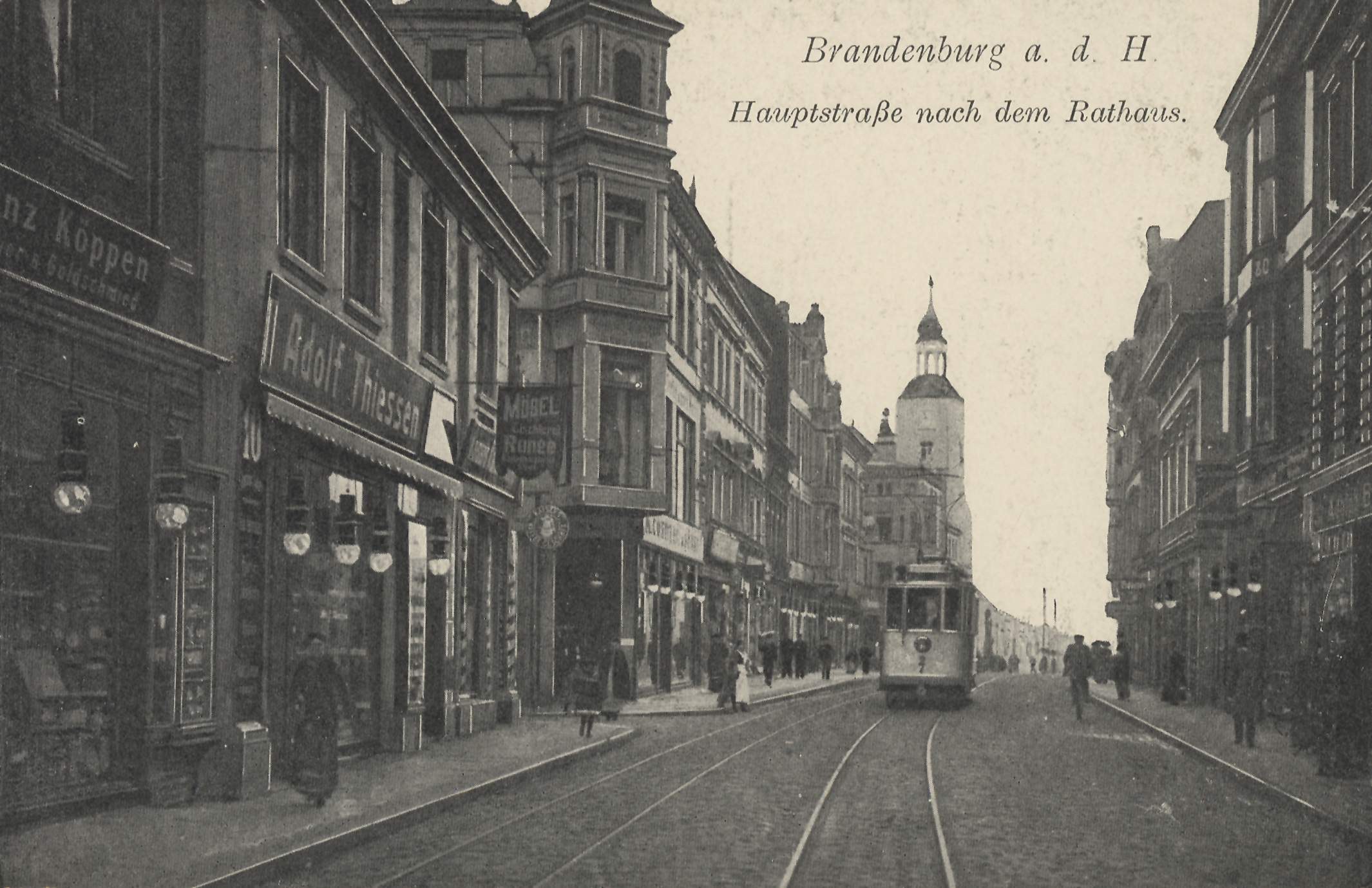 Ein altes Schwarz-Weiß-Foto einer Stadtstraße in Brandenburg, Deutschland, mit einer Straßenbahn auf den Schienen, Menschen auf dem Gehweg, Gebäuden mit Fenstern, Schildern und Straßenlaternen unter einem bewölkten Himmel.