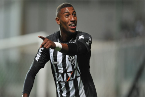 Ein Fußballspieler in einem schwarz-weißen gestreiften Trikot lächelt, während er ein Tor feiert, mit einem unscharfen Hintergrund, um den Moment zu betonen.