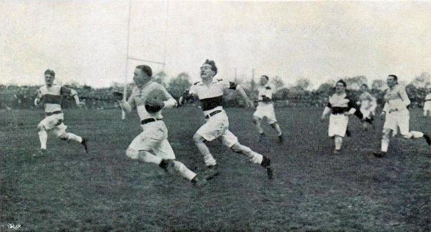 Schwarzes und weißes Bild von Männern, die Rugby auf einem grasbewachsenen Feld mit Bäumen und Pfählen im Hintergrund spielen, beschriftet mit "1930er Jahre Rugby."