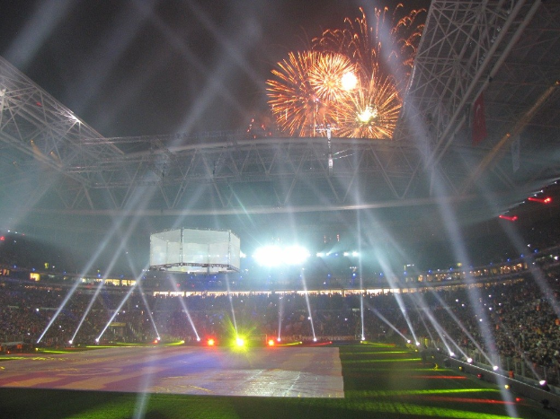 Olympiastadion in London bei Nacht, hell erleuchtet mit grünem Gras, umgeben von einer großen Menge und Feuerwerk, das den Himmel erhellt.