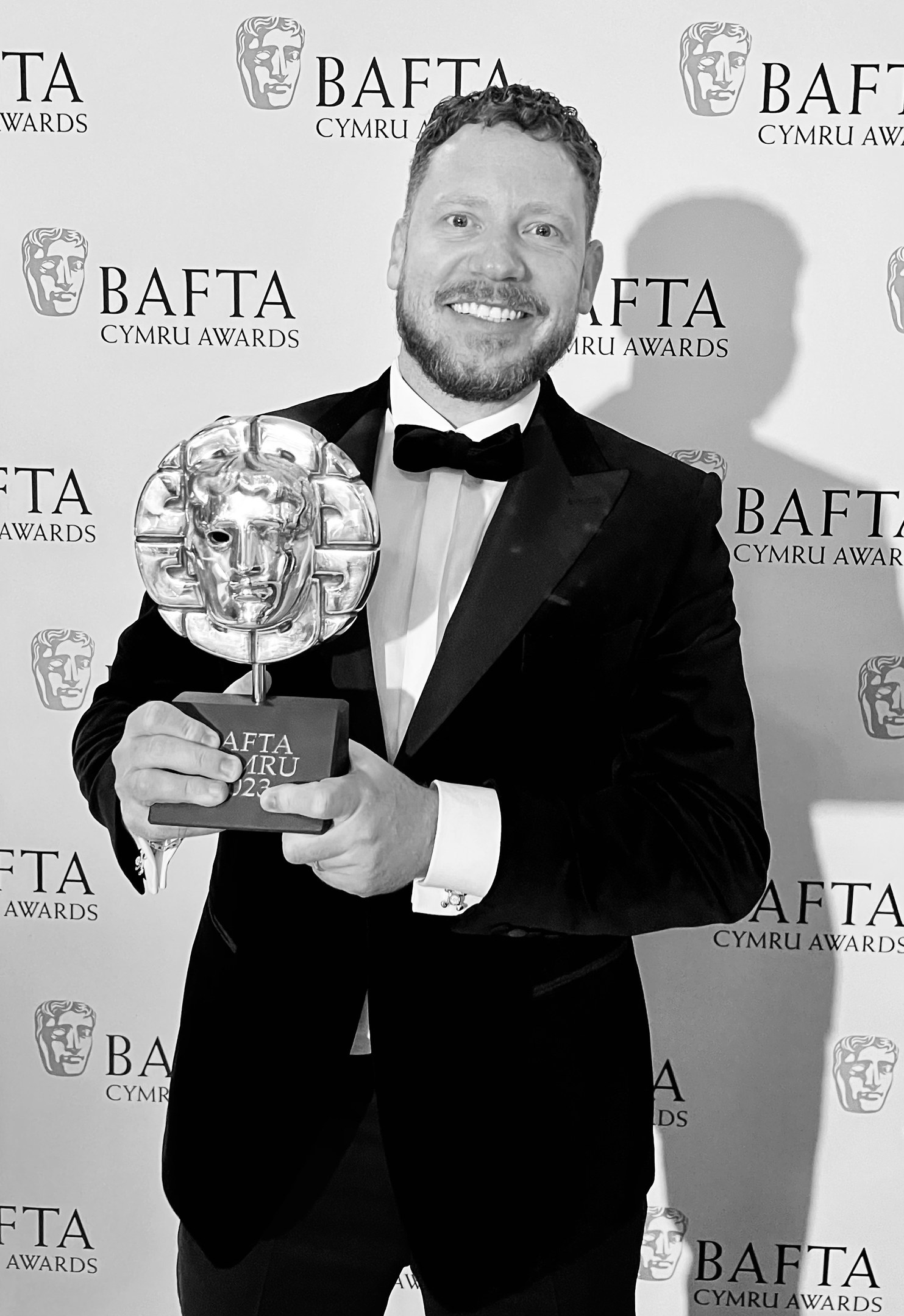 Ein Mann in einem Smoking, der eine BAFTA-Auszeichnung hält und lächelt, mit einem Hintergrundplakat, auf dem "BAFTA Awards 2018" steht.
