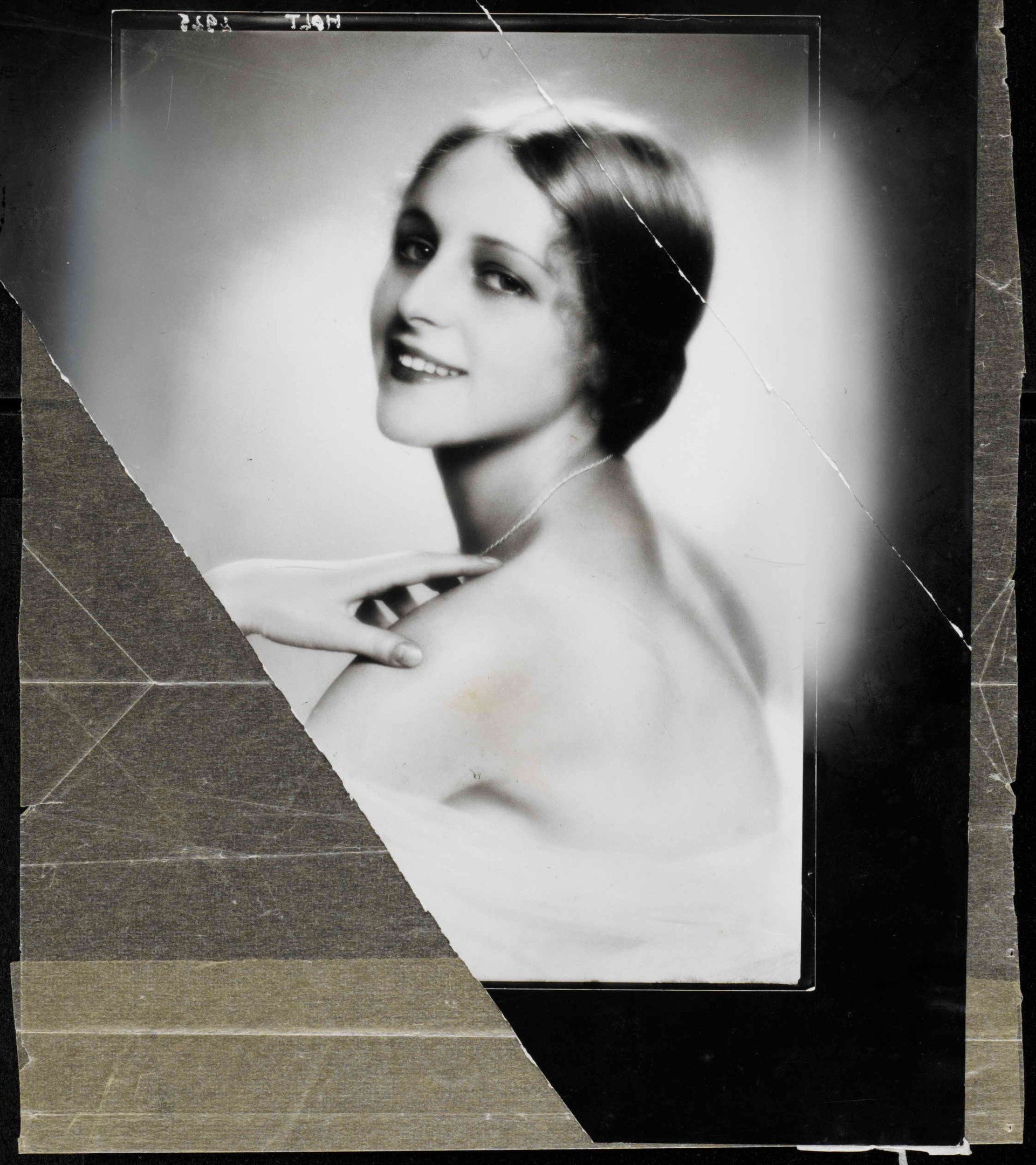 Schwarz-weißes Foto einer Frau in einem Kleid mit einer 1920er-Jahre-Frisur, die direkt in die Kamera lächelt.