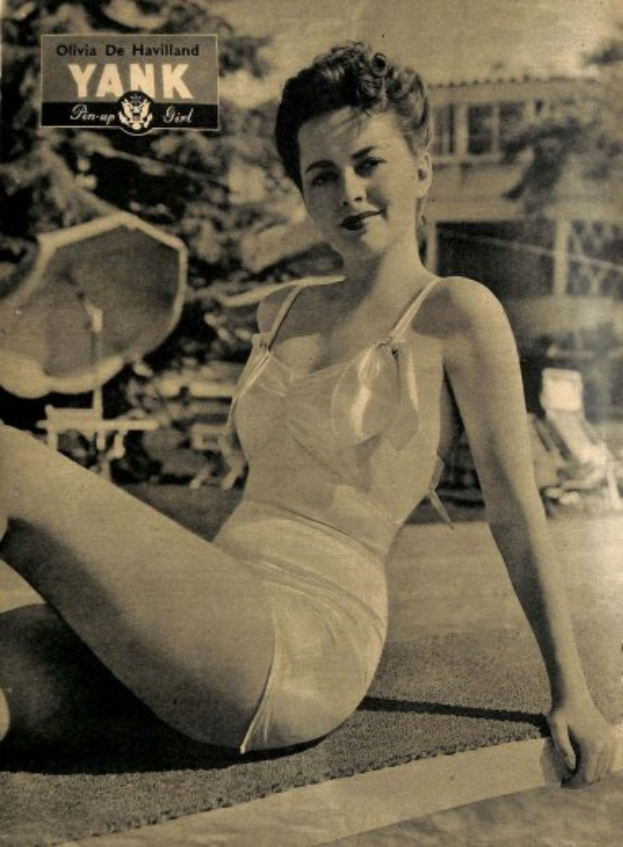 Olivia de Havilland in einem Bikini sitzend auf dem Boden und strahlend, mit Bäumen, Stühlen, einem Gebäude und Text im Hintergrund.