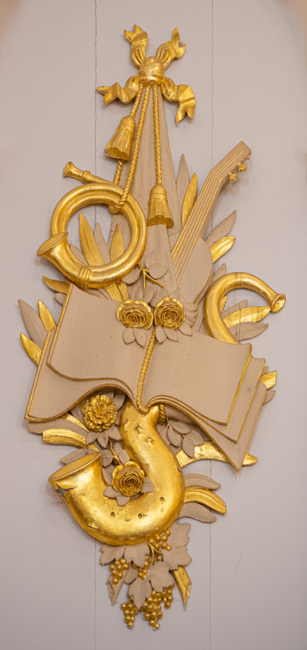 Goldene Skulptur einer musikalischen Instrumentenanordnung an einer Wand, mit einer zentralen Gitarre flankiert von Saxophonen und Schlagzeug.