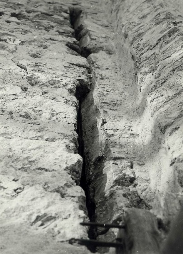 Schwarz-weiß-Foto eines große Risses im Boden eines Kanals mit einem sichtbaren Wasserzeichen auf der linken Seite.