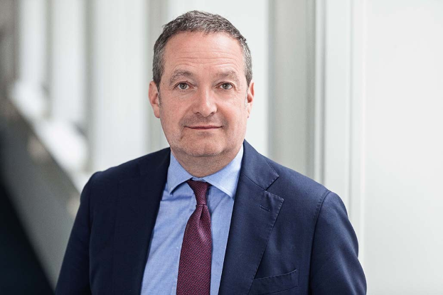 Ein Mann im Anzug steht vor einem Fenster in einer professionellen Umgebung und zeigt damit an, dass er der neu ernannte CEO ist.