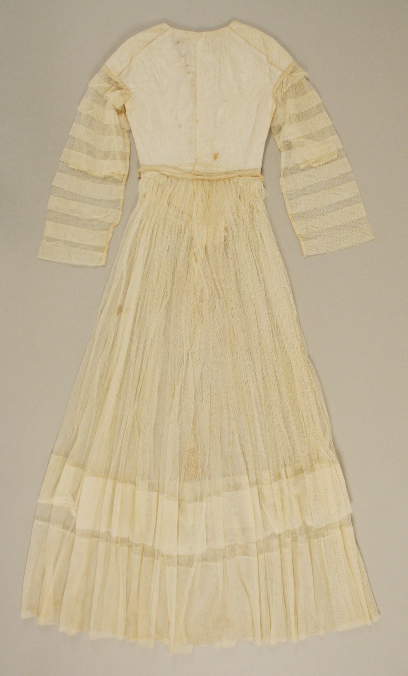 Ein weißes, langärmliges Kleid mit einer gerüschten, bodenlangen Schleppe und einem dezenten Schimmer auf einer weißen Oberfläche.