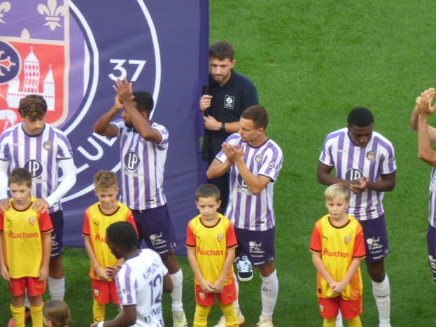 Gruppe junger Jungs auf einem Fußballfeld, die klatschen, mit einem Banner und Logos im Hintergrund auf grünem Gras.