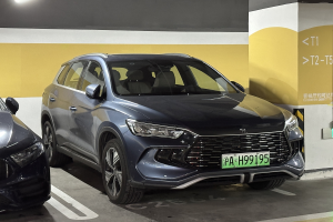 Zwei Autos nebeneinander in einer überdachten Garage mit einer Wand und einer Deckenbeleuchtung im Hintergrund, begleitet von einem Schild auf Chinesisch auf der rechten Seite.
