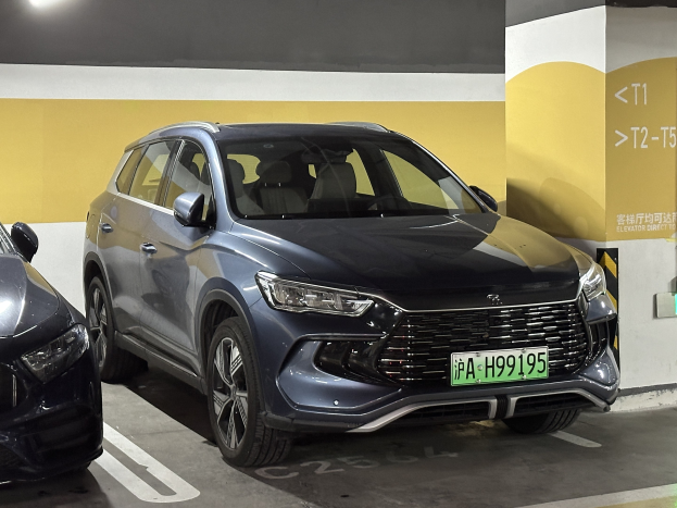 Zwei Autos nebeneinander in einer überdachten Garage mit einer Wand und einer Deckenbeleuchtung im Hintergrund, begleitet von einem Schild auf Chinesisch auf der rechten Seite.
