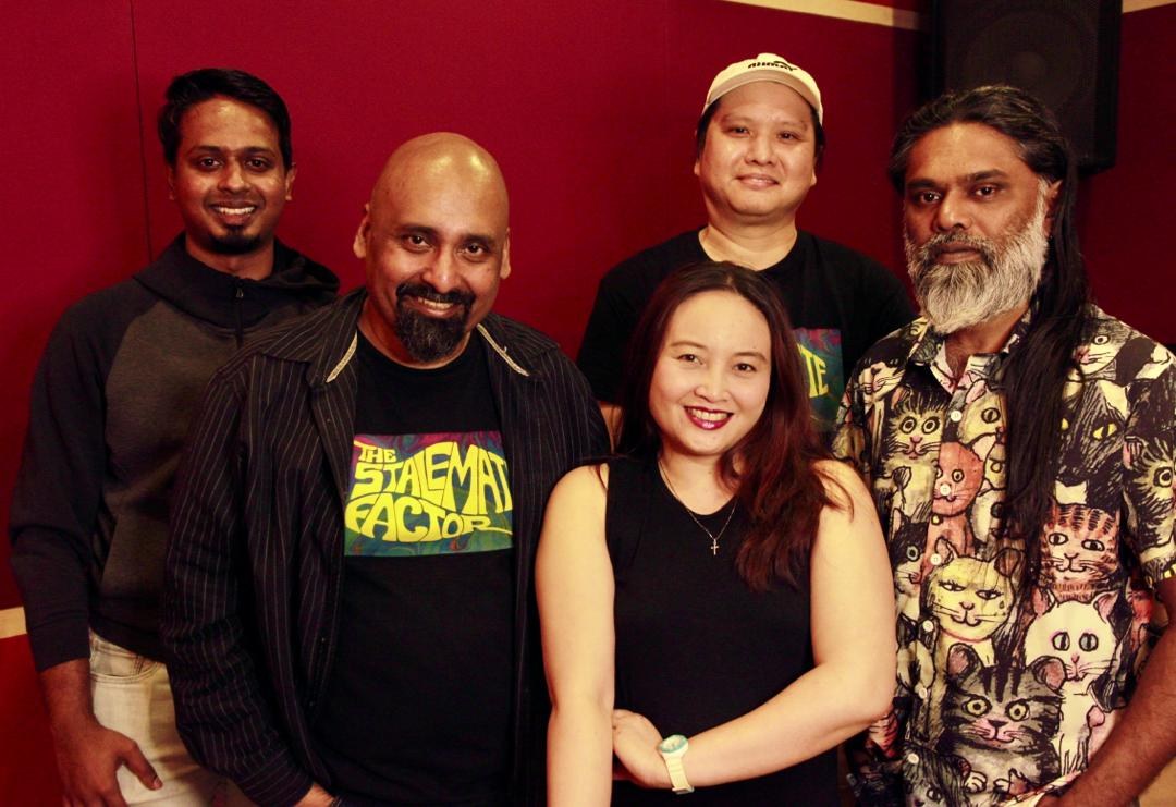 Eine Gruppe von Menschen, die zusammen in einem Aufnahmestudio stehen, lächeln und locker gekleidet sind, mit ihren Armen umeinander.