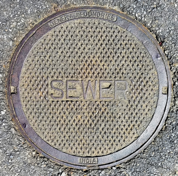 Metallschachtdeckel auf der Straße mit dem Wort "Kanal" geprägt.