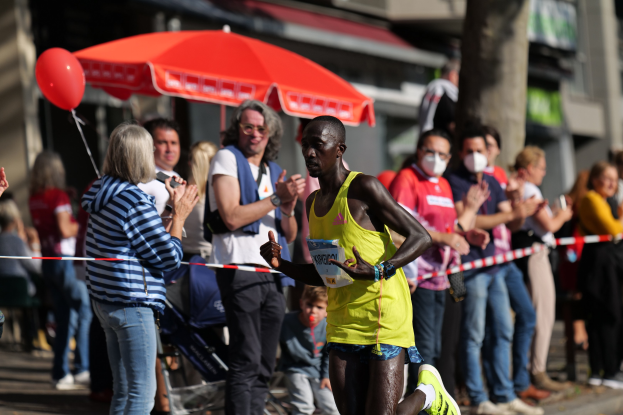 Ein Mann in einem gelben T-Shirt läuft durch eine Zuschauermenge bei einem Marathon, während die Zuschauer im Hintergrund klatschen und jubeln.