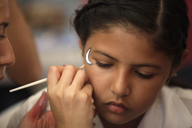 Ein Make-up-Artist trägt Make-up auf das Gesicht eines jungen Mädchens auf, während der Hintergrund unscharf ist.
