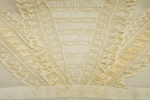 Nahaufnahme eines weißen Kleides mit zarter, detailreicher Spitzenverzierung auf einem leichten, luftigen Stoff.