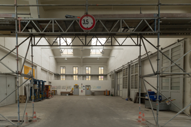 Lagerhalle mit Gerüsten, Verkehrszeichen, Metallstangen, einem Schild, Maschinen, einer Tür, Fenstern, einer Wand, Deckenleuchten und einem Dach.