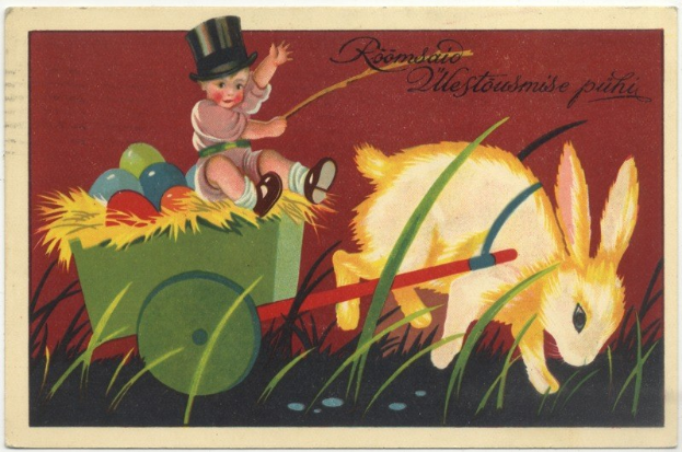 Alte Postkarte mit einem Baby in einem Zylinder, das einen mit bunten Ostereiern gefüllten Handkarren schiebt, begleitet von einem Hasen, mit handgeschriebener Text, der einen glücklichen Osterwunsch aussprechen.