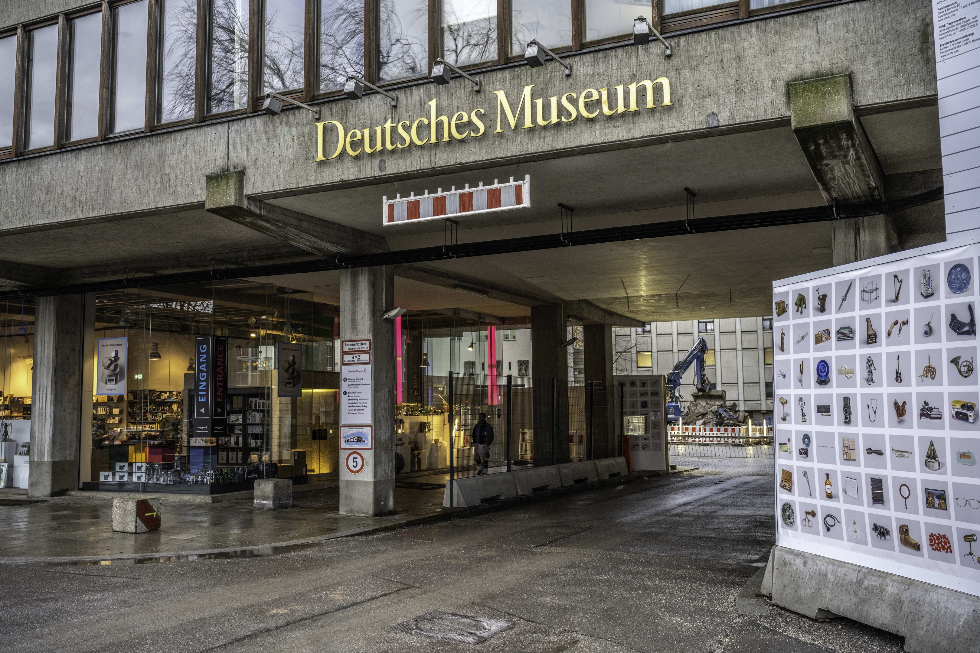 Außenansicht des Deutschen Museums in Berlin: großes Gebäude mit Glasfenstern, Säulen und Namensschild, daneben Informationsschild, Bäume, andere Gebäude und Himmel im Hintergrund.