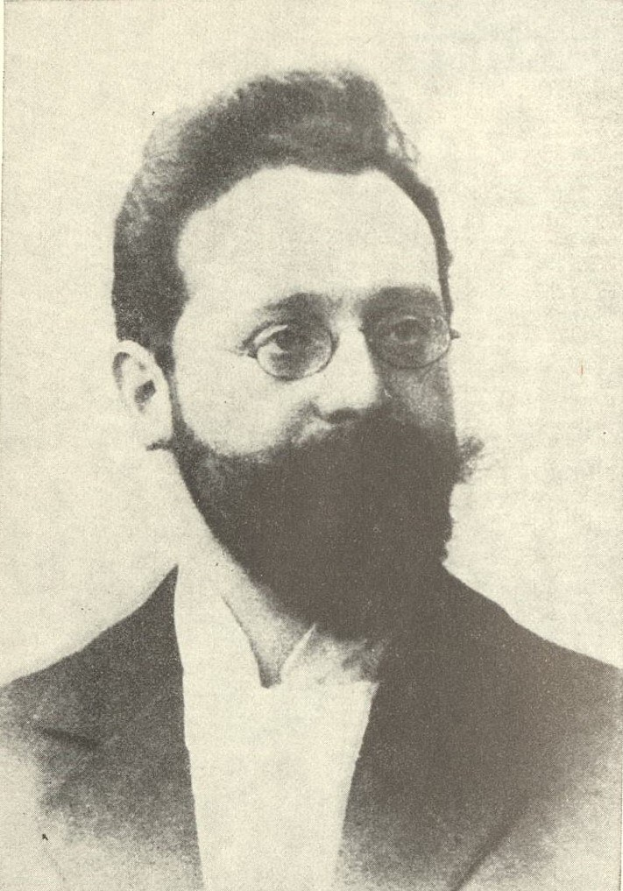 Schwarzes und weißes Porträt eines bärtigen Mannes in Anzug und Krawatte mit ernstem Gesichtsausdruck, konzentriertem Blick und ordentlich frisiertem Haar und Bart.