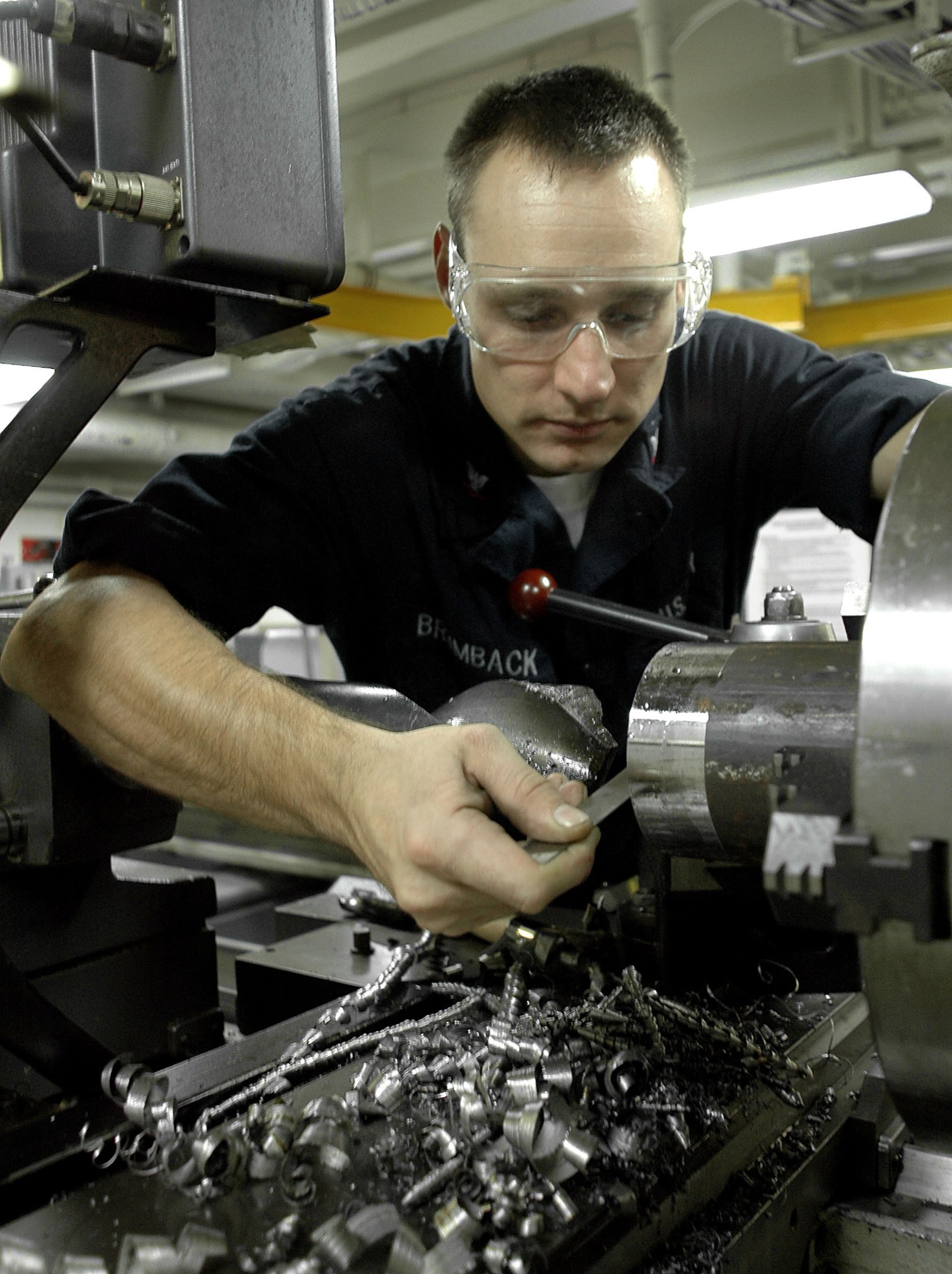 Ein Fräser mit Schutzbrille bedient eine Maschine in einer gut beleuchteten Fabrikumgebung.