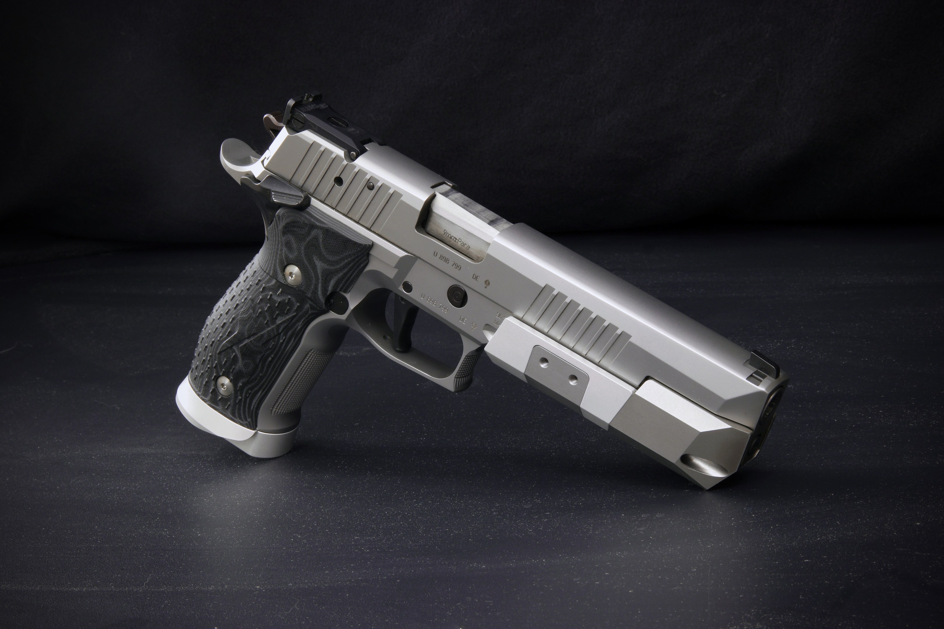 Eine Sig Sauer P226 X-Five 9mm Pistole auf einer schwarzen Oberfläche mit einem schwarzen Hintergrund.