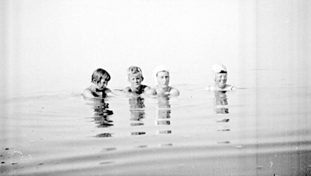 Vier Kinder mit Schwimmkappen schwimmen gemeinsam in einem schwarz-weißen Pool.