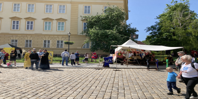 Eine Gruppe von Menschen geht eine Kopfsteinpflasterstraße in Krakau, Polen, mit Zelten, Tischen und einem Gebäude mit sichtbarem Text im Hintergrund.