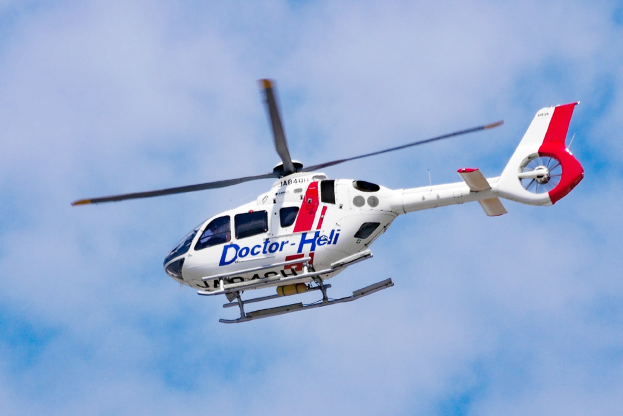 Weißer und roter medizinischer Hubschrauber fliegt durch einen blauen Himmel mit Wolken im Hintergrund.