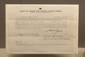 Ein Blatt mit dem Text "Dienstpflicht für US-Richter" darauf, das auf einem Tisch vor einer Wand liegt.