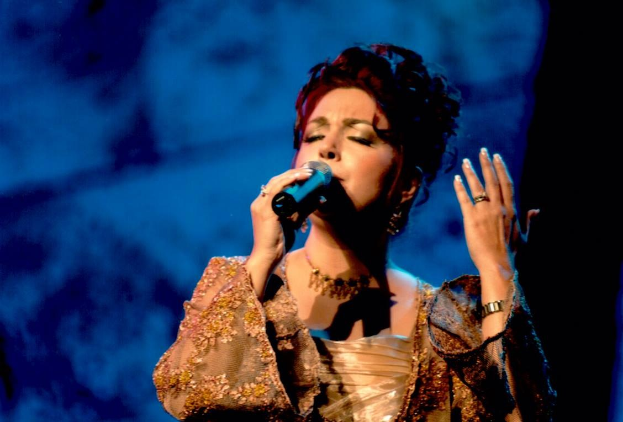Frau in goldenem Kleid singt auf der Bühne der Eurovision Song Contest mit blau-schwarzem Hintergrund.