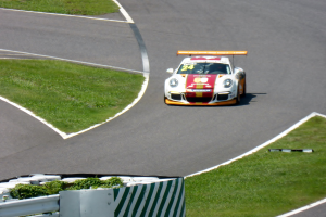 Ein Porsche 911 GT3 RSR auf der Nürburgring 24 Stunden Rennstrecke, umgeben von grünem Gras und einem Geländer, mit seinen leuchtenden Farben und seiner eleganten Form.
