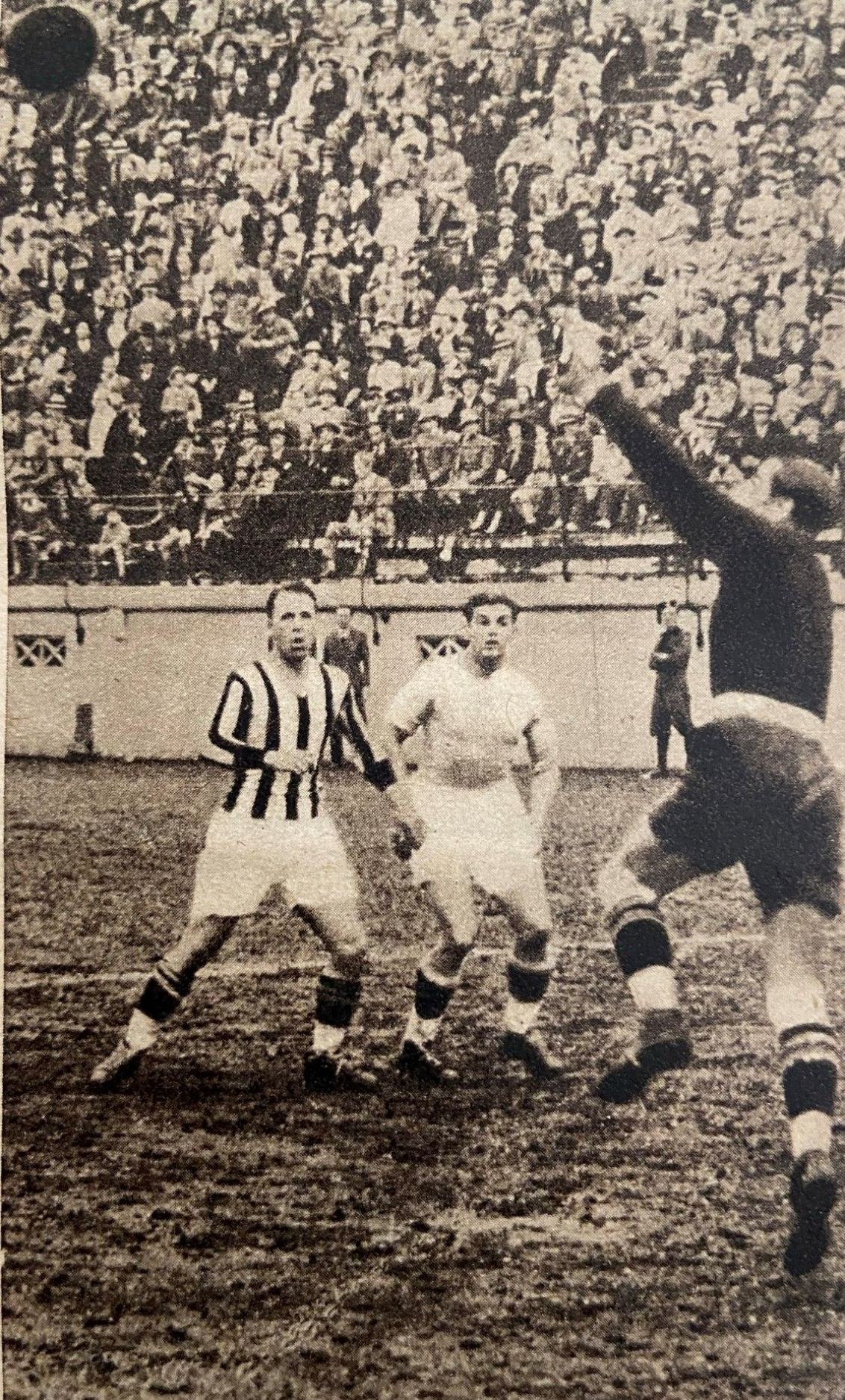 Schwarz-weißes Foto von Männern, die Füßball spielen, mit Zuschauern auf der Tribüne und einer Wand im Hintergrund, beschriftet mit "Newcastle United v West Bromwich Albion".
