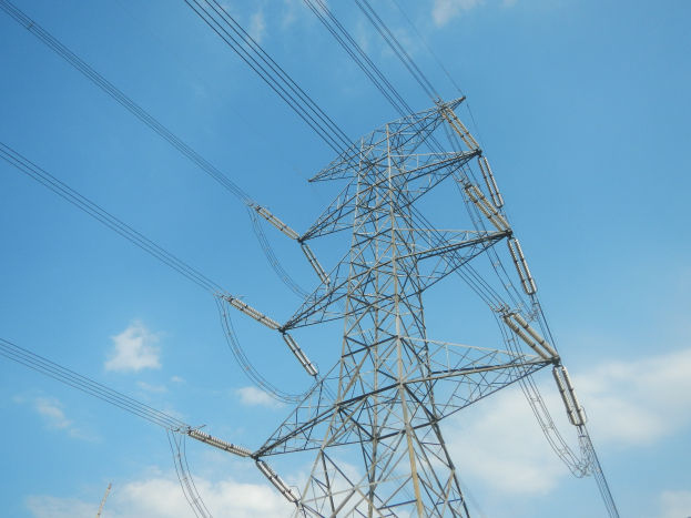 Hochspannungsfreileitungen erstrecken sich von einem Turm gegen einen blauen Himmel mit Wolken.
