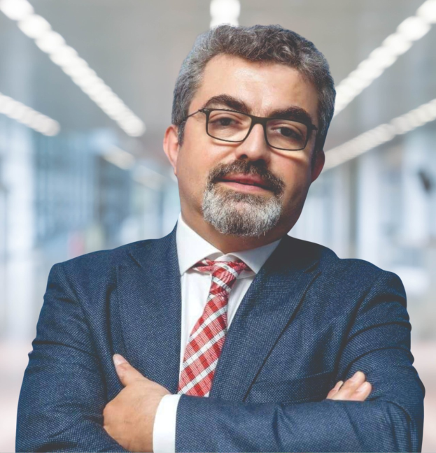 Ein Mann im Anzug und mit Krawatte, der die Arme verschränkt und eine Brille trägt, steht vor einem unscharfen Hintergrund mit Text, der ihn als neu ernannten Marketingchef identifiziert.