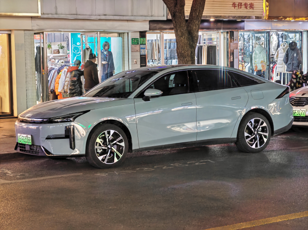 Ein Mitsubishi Lancer EV Elektroauto, das nachts auf einer Straße geparkt ist, umgeben von Gebäuden, Geschäften, Schaufensterpuppen, Schildern und Lichtern.