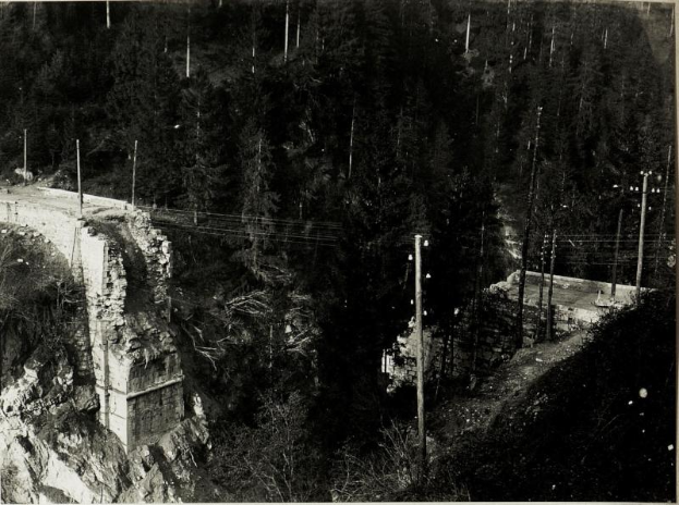 Ein Schwarz-Weiß-Foto einer Brücke über einen Fluss während ihrer 1930er-Jahre-Bauarbeiten, mit Bäumen, Pfählen und Felsen im Hintergrund.