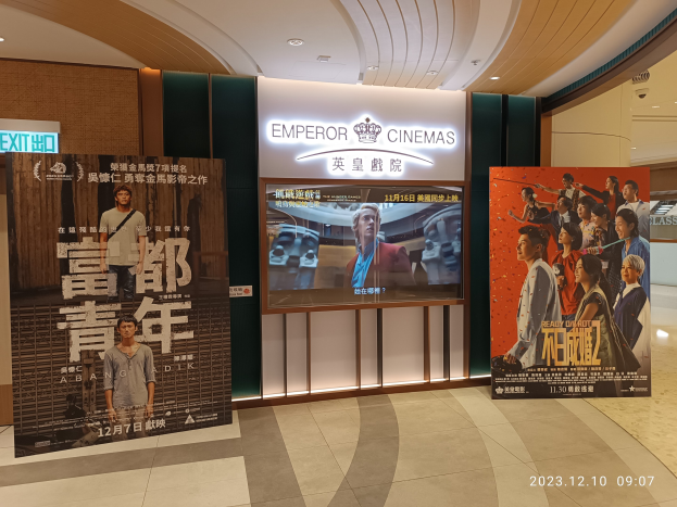 Eintritt zum Emperor Cinema in Hong Kong mit Bannern, einem Bildschirm, einer Namensschild, Deckenleuchten und einem Wasserzeichen.