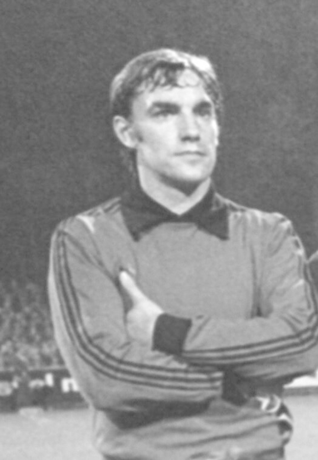 Schwarzes und weißes Foto eines Mannes auf einem Fußballfeld mit verschränkten Armen, umgeben von sitzenden Zuschauern, der als legendärer Torwart von Manchester United gilt, der im Alter von 89 Jahren starb.