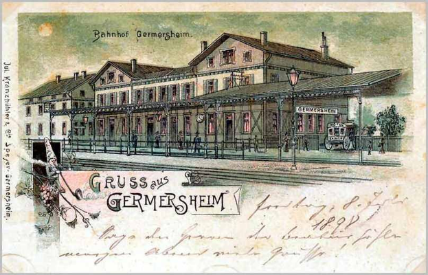 Schwarz-weiß-Postkarte des Bahnhofs Germersheim in Deutschland, die ein Gebäude mit Fenstern, einen Zaun, einen Straßenmast, Menschen, Fahrzeuge, Bäume und einen bewölkten Himmel zeigt.