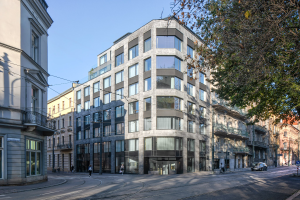 Großes Bürogebäude mit zahlreichen Fenstern, umgeben von Straßeninfrastruktur, Fahrzeugen, Fußgängern, Bäumen und einem bewölkten Himmel als neue Hauptzentrale.