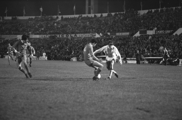 Schwarze-Weiß-Foto von Männern, die Fußball in einem Stadion mit Zuschauern und Fahnen im Hintergrund spielen.