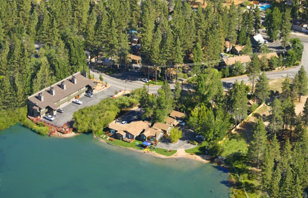 Luftbild eines Resorts am Seeufer, umgeben von Bäumen, Häusern, Fahrzeugen, Straßen, Masten und Gras, mit dem See unten.