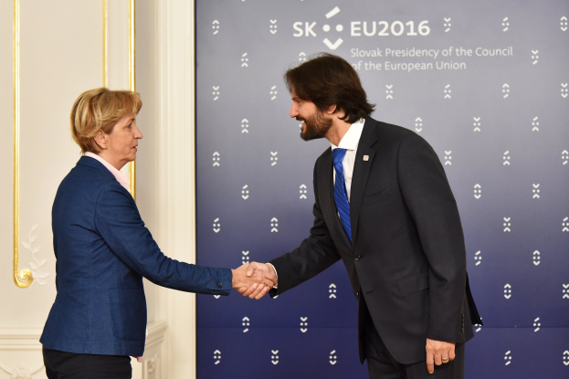 Bundeskanzlerin Angela Merkel und Bundeskanzler Joachim Gauck schütteln sich die Hände vor einem "EU-Gipfel"-Plakat und lächeln freundlich.